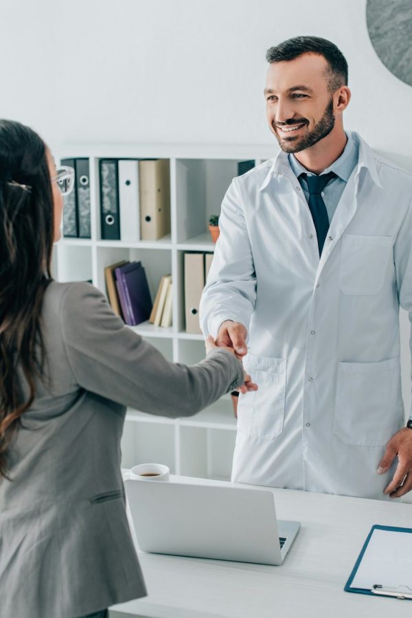 patient and smiling doctor shaking hands in clinic