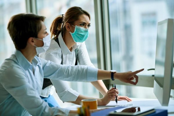 young-businesswoman-her-colleague-wearing-face-masks-while-working-computer-office-virus-epidemic_637285-5274